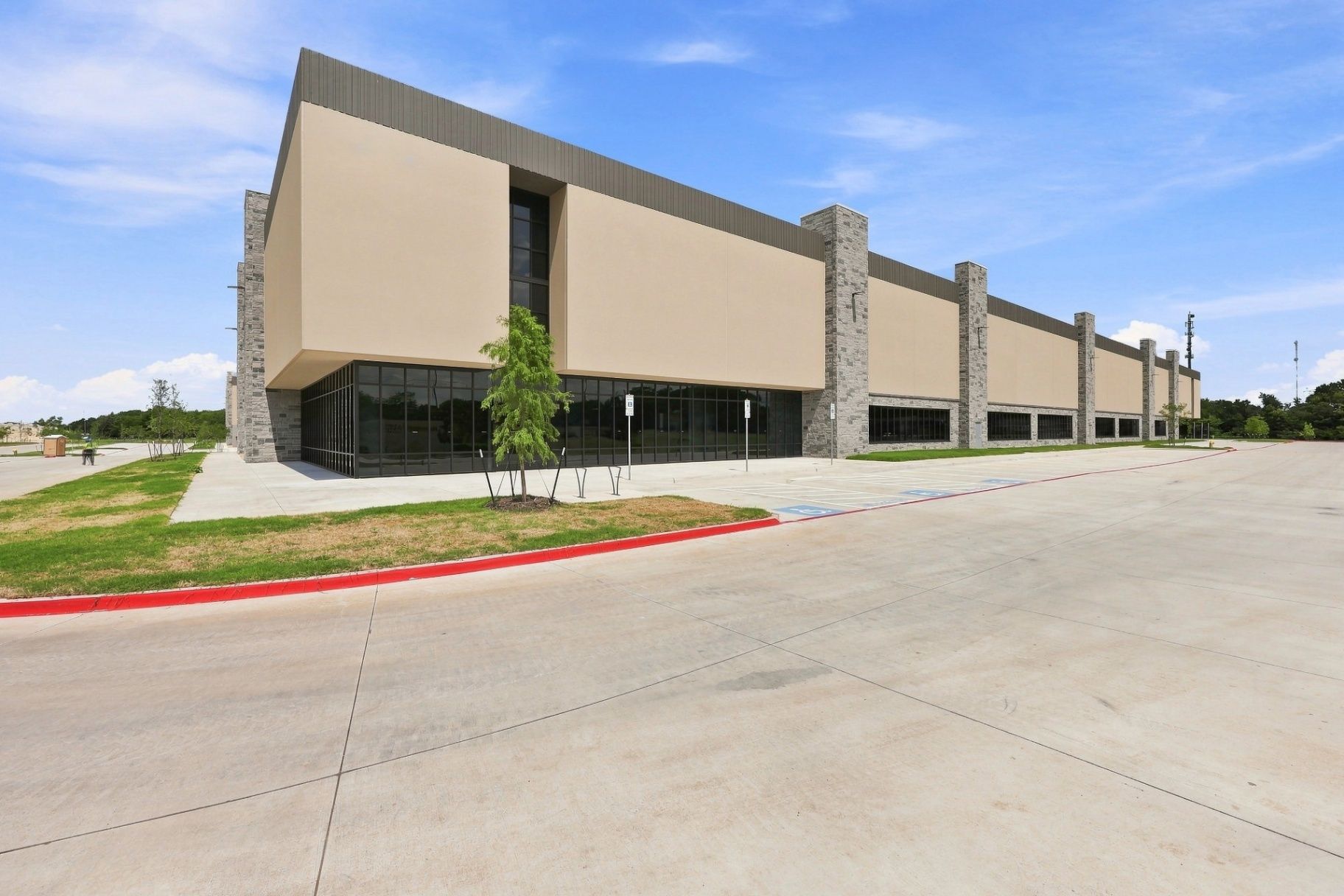 Wide exterior view of a commercial warehouse with façade, windows, entrance area, and parking surface