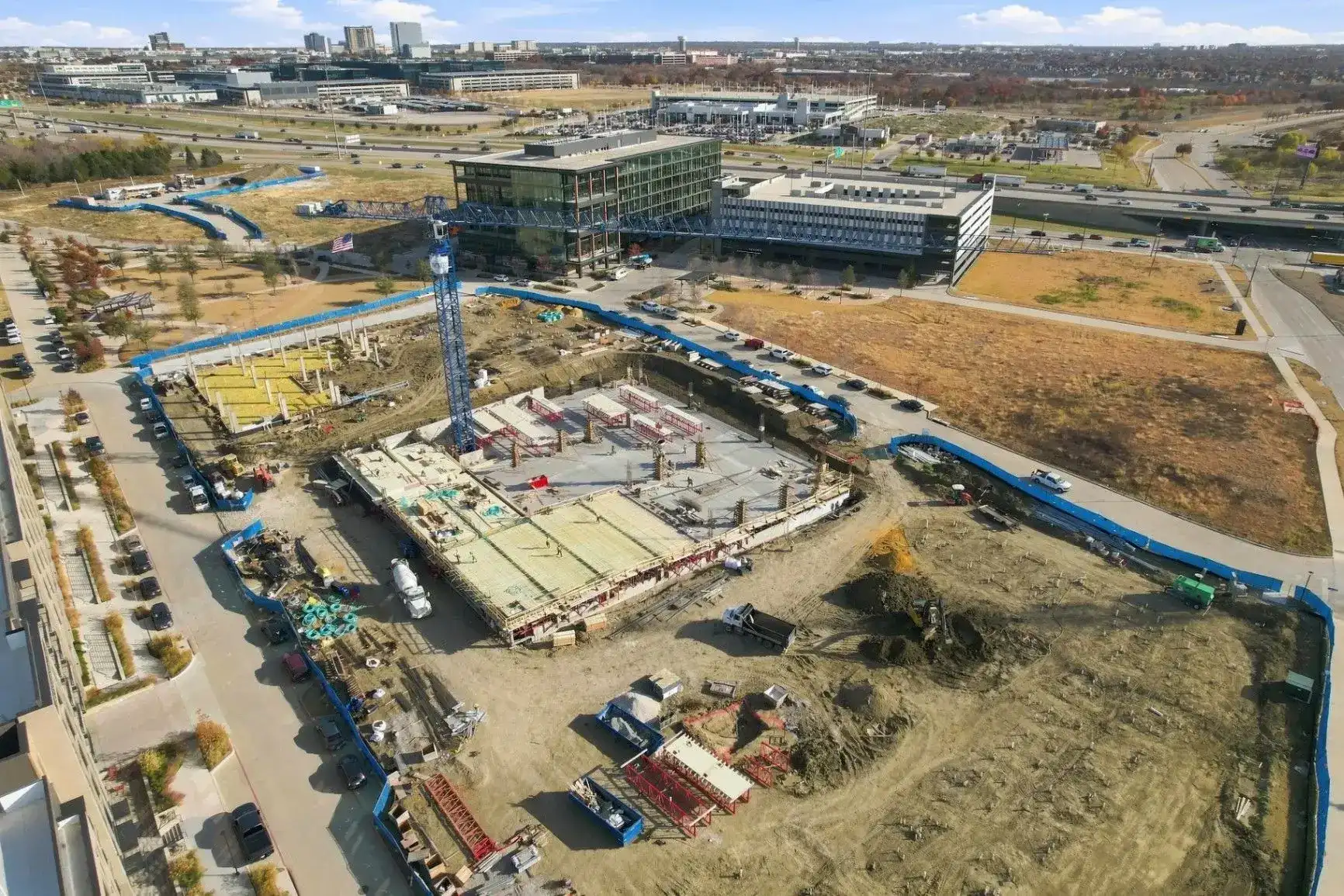 Aerial view of an active construction site with a crane, surrounding buildings, and roadways