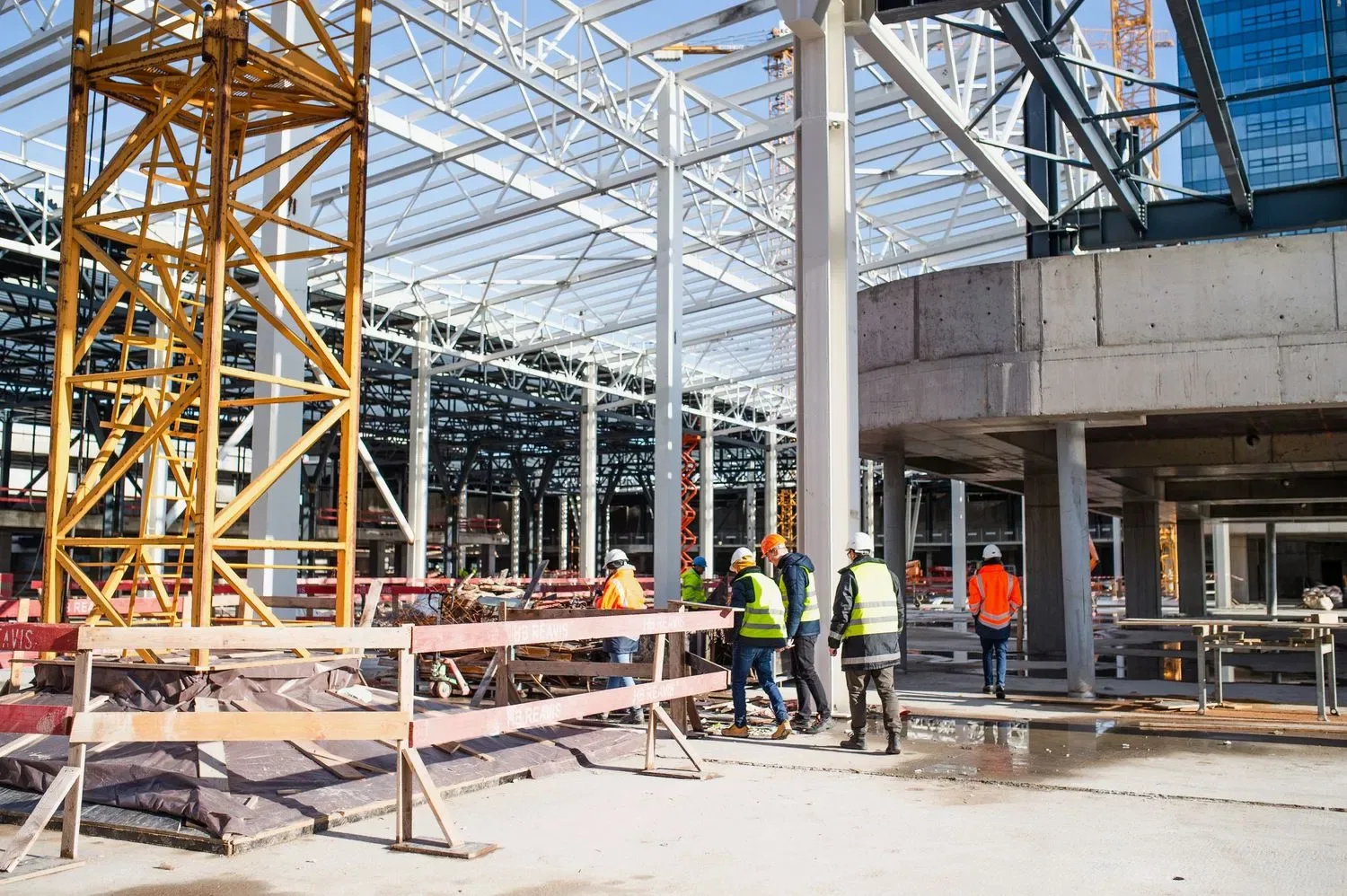 Construction team conducts an on-site walkthrough beneath a steel framework and concrete structure, documenting project progress.